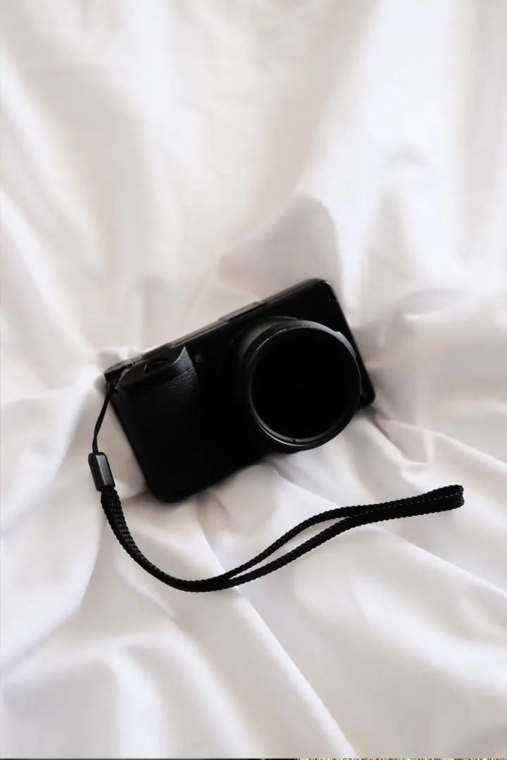 Kompaktkamera mit dunklem ND-Filter auf dem Objektiv, auf weißem Stoff liegend