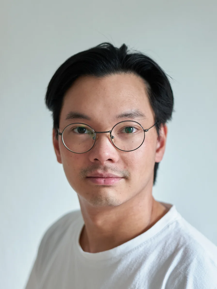 Echtes, unbearbeitetes Portraitfoto eines Mannes mit runder Brille im weißen T-Shirt vor heller Wand